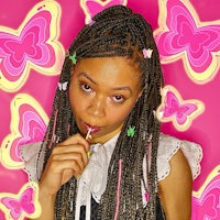 a girl with braided hair blowing a bubble on a pink background