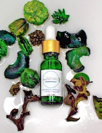 a bottle of oil surrounded by green leaves and mushrooms