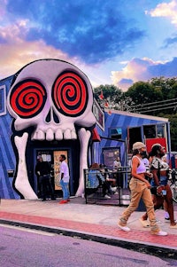 people walking past a colorful building with a skull on it