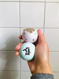 a person holding three bath bombs in front of a tiled wall